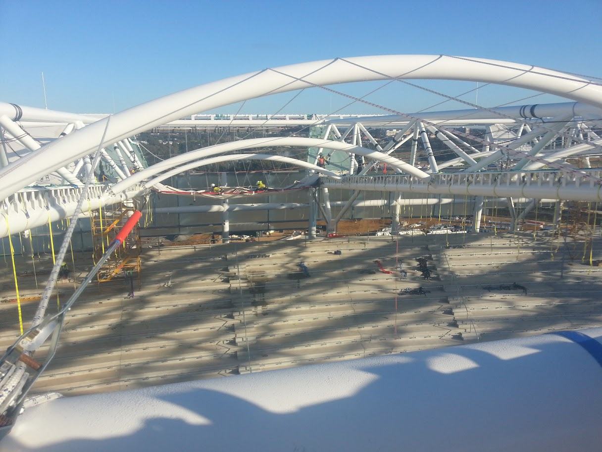 Sweeping white roof arches and steel framework above a stadium build, seen from the roof edge