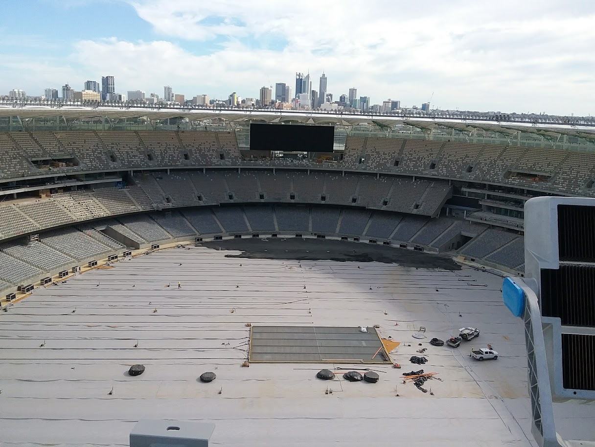 Stadium seating bowl under construction seen from the roof, with a city skyline on the horizon
