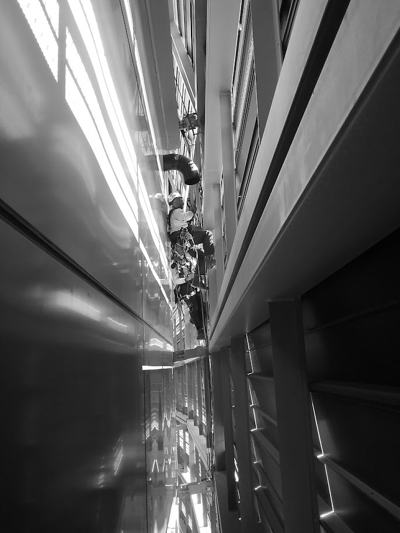 Black-and-white view of a rope access technician working in a narrow shaft between two building façades