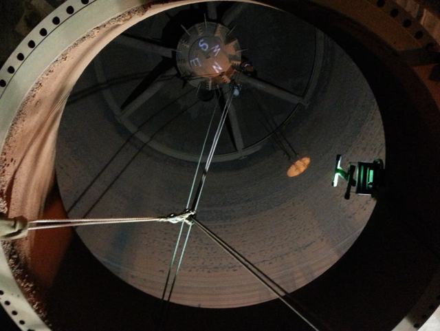 Looking straight up inside a tall steel silo, with rope access lines rigged from the top hatch down the inside wall