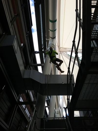 Rope access technician in hi-vis suspended beside a stadium column, next to the roof membrane