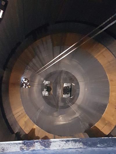 Looking down into a large circular steel tank, with rope access technicians working on rope far below
