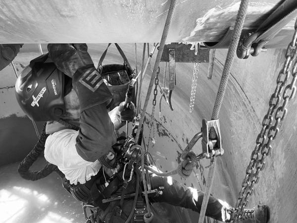 Rope access technicians rigged with ropes and chains inside a tank, viewed from above